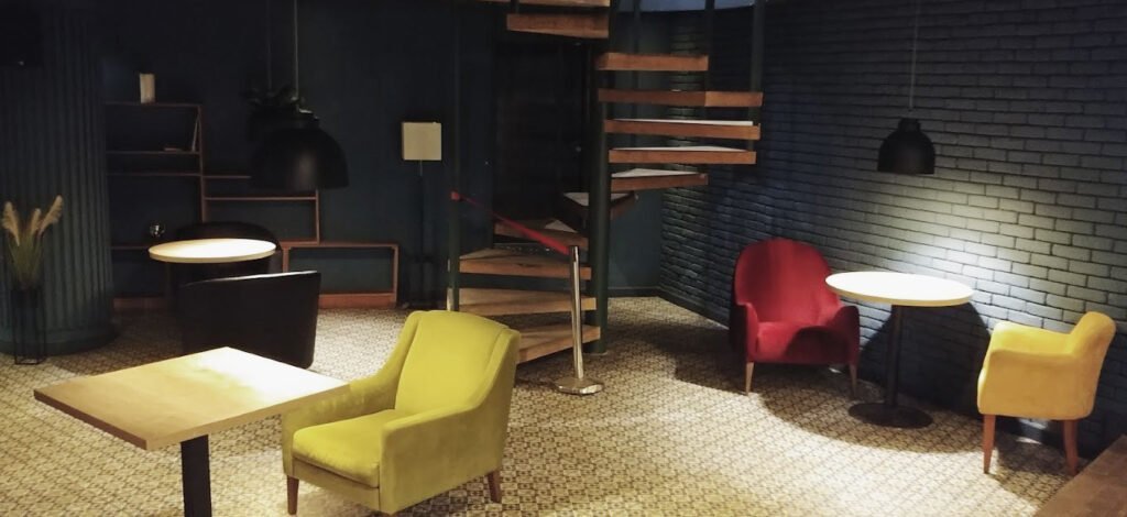 Cosy lounge corner in the Amirani Cinema in Tbilisi with yellow and red armchairs, small tables and a spiral staircase in the background.