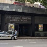 "Amirani Cinema in Tbilisi, Georgia: A modern cinema building with a police car in front of it, surrounded by trees and posters of current films."