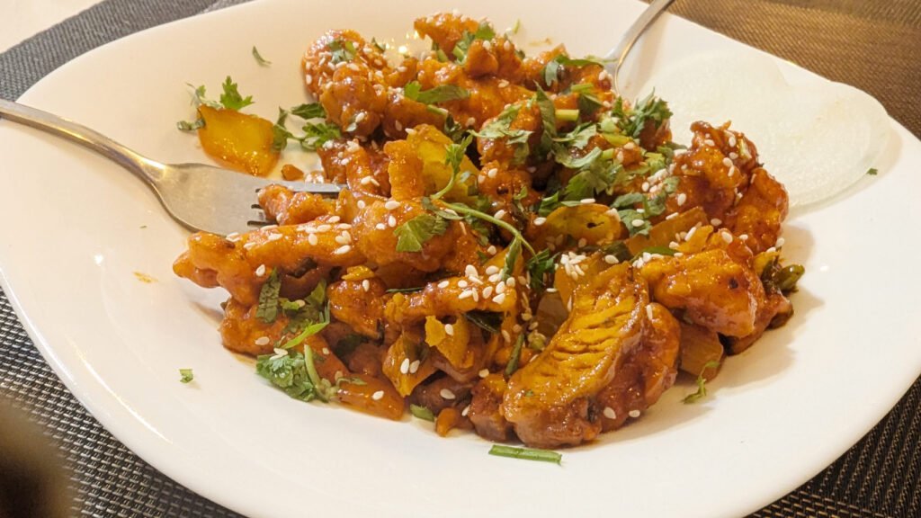 A close-up of golden-brown, crispy fried chicken pieces, with visible herbs and spices on the breading