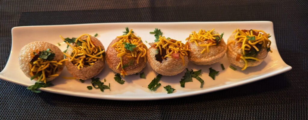 A close-up photo of several pani puri, a popular Indian street food. The crispy, hollow puri shells are filled with a mixture of potatoes, chickpeas, and spices, and are served with a tangy tamarind water.